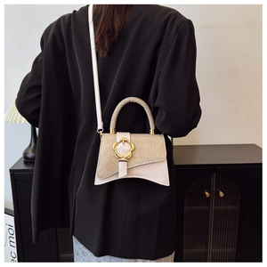 Dettaglio di una borsa chic color crema con chiusura a fiore dorato su una giacca blazer