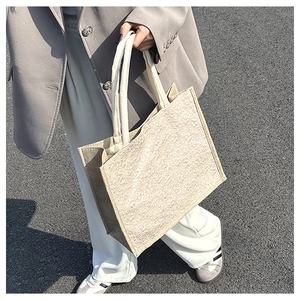 Detail of a large beige textured woven tote bag held by a model in casual chic attire
