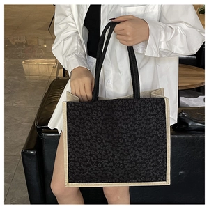 Close-up of linen tote bag with floral pattern, black rope handles, and woven trim detail