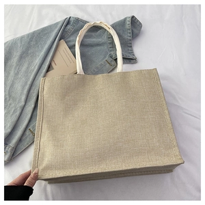 Detail of a large jute tote bag with white braided rope handles on a fabric background