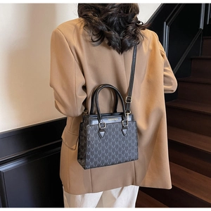 Detail shot of the dark grey tote bag with monogram print worn with a camel blazer