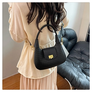 Detail view of black woven texture handbag with golden hardware worn on a model's shoulder