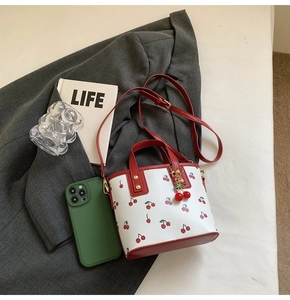Détail du sac seau blanc avec imprimé cerise, bordure rouge et pendentif cerise