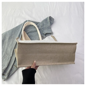 Detail of the wide base and white cotton rope handles on the beige linen tote bag