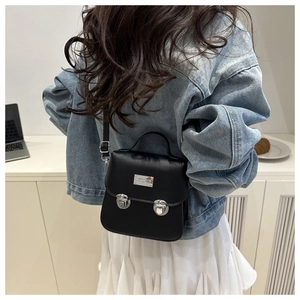 Détail du petit sac carré noir avec boucles métalliques rétro et poignée sur le dessus