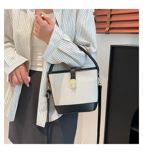 Detail of contrast stitch bucket bag featuring woven fabric, black trim, and gold clasp
