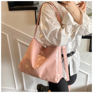 Detail of light pink patent leather tote bag with glossy finish and gold logo plate