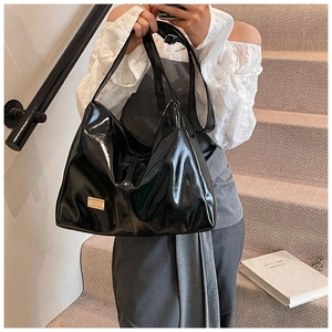Close-up of black glossy patent leather tote bag with gold metal logo and adjustable strap