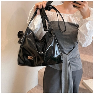Detail of glossy black patent leather shoulder tote bag with a golden metal logo plaque