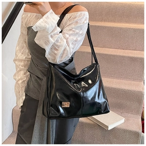 Detail of glossy black patent leather hobo bag with a rectangular metal logo plaque