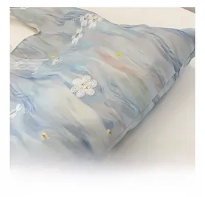 Close-up of floral embroidery and white lace edging on a watercolor blue canvas tote bag
