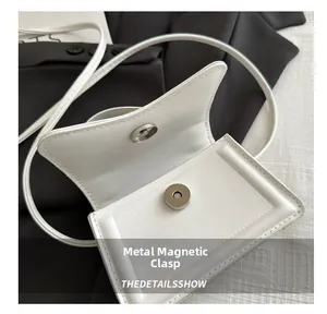 Detail view of the silver hardware magnetic buckle on a white leather flap square bag