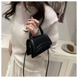 Close-up of a minimalist black crossbody bag with wave-edge flap and metal hardware