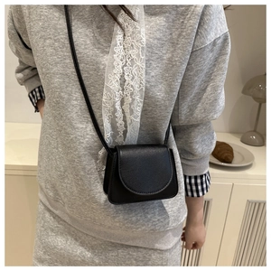 Detail of a black pebbled leather crossbody bag shown in a stylish minimalist setting