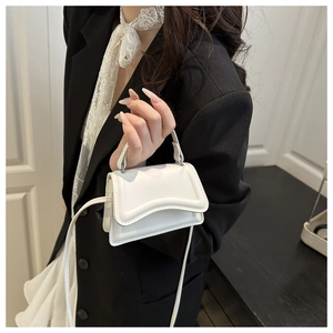 Dettaglio mini borsa bianca con bordo ondulato indossata su un blazer nero di tendenza