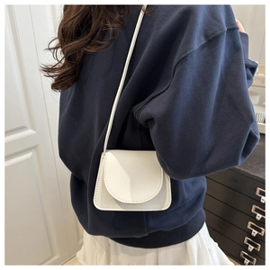 Close-up of a white minimalist saddle crossbody bag with litchi texture on a model