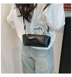 Detail of a black leather crossbody bag with a unique silver streamlined metal handle