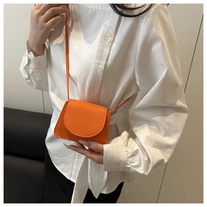 Detail of an orange mini crossbody bag with litchi grain texture on a white shirt