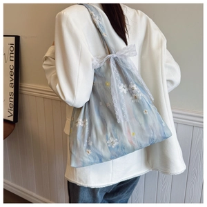 Detail of light blue floral tote bag with white lace bow and elegant embroidery