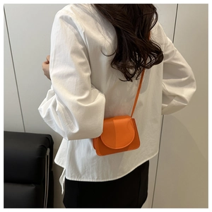 Detail of bright orange textured mini crossbody bag worn by model in a minimalist setting