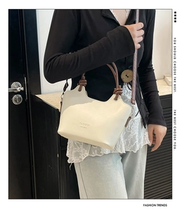 Detail of cream PU leather bucket bag featuring round brown handles and fashion lettering