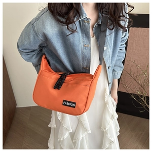 Detailaufnahme der orangefarbenen Nylon-Umhängetasche mit Fashion-Label und Tragegurt