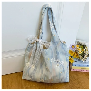 Detail of light blue tote bag featuring 3D white flower embroidery and a lace bow accent