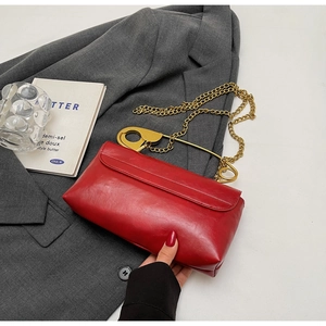 Macro view of a red patent leather bag featuring a gold safety pin handle and chain strap