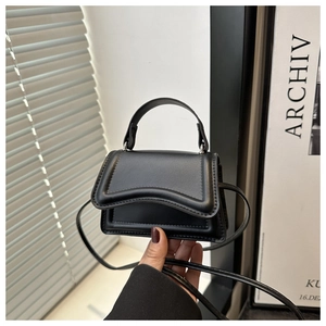 Dettaglio di una mini borsa in pelle nera con patta curva e tracolla sottile