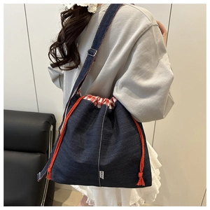 Detail of blue denim bucket bag with red drawstring closure and white fashion label