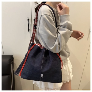 Detail of dark blue denim drawstring crossbody bag with red plaid lining and strap