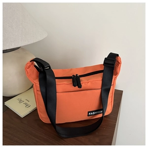 Detail einer leuchtend orangefarbenen Nylon-Umhängetasche mit Label und schwarzem Gurt