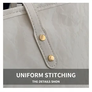 Dettaglio di cuciture uniformi e rivetti dorati su borsa tote in pelle color crema