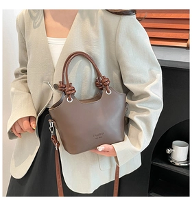 Detail view of brown leather handbag featuring knotted handle and wave-shaped opening