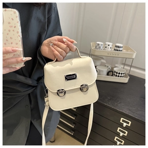 Detail view of cream leather handbag featuring silver metal buckles and top handle
