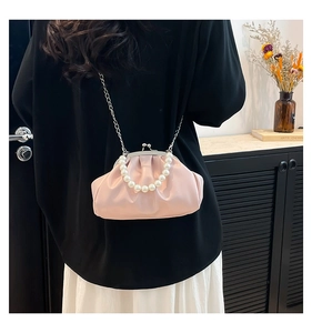 Pink pleated dumpling bag with large pearl handle and silver chain strap on a shelf