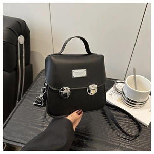 Détail d'un mini sac bandoulière noir avec double fermoir argenté sur table en bois