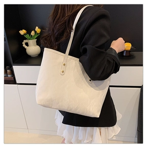 Detail of white textured tote bag with gold rivets worn on shoulder by model