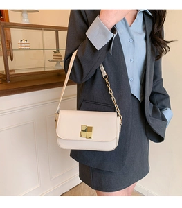 Detail of cream white leather handbag with gold buckle and chain strap on a model