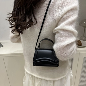 Borsa nera minimalista con patta curva e manico superiore in un ambiente elegante bianco