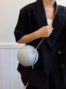 Silver spherical clutch with gold chain strap worn over a black blazer for a modern style