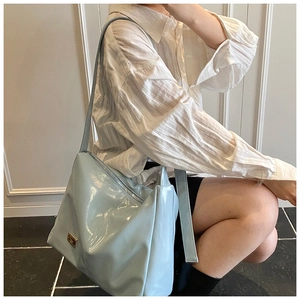 Detail of light blue glossy tote bag with metal logo worn by a model in a casual outfit