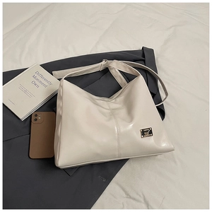Close-up of a cream faux leather tote bag with a metal logo plate on a messy bed
