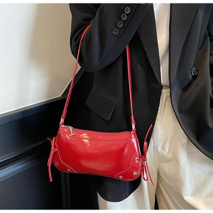 Macro view of bright red patent leather texture and silver rivet details on baguette bag