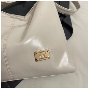 Detailed close-up of cream leather shoulder bag with engraved golden metal logo plate