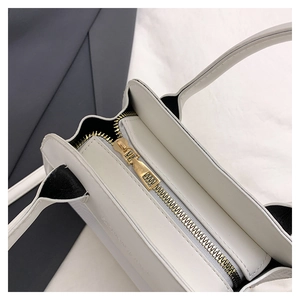 Dettaglio della borsa in pelle bianca con cerniera dorata e stampa del marchio