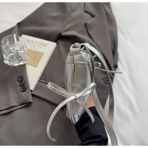 Detail of silver metallic shoulder bag showing side profile and elegant bow accent