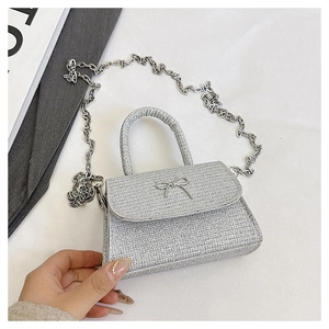 Detail of silver glitter mini handbag featuring a metallic bow and chain strap