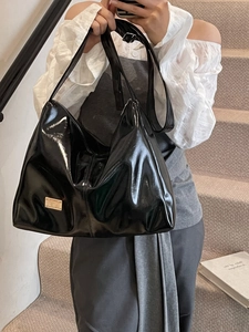 Minimalist black patent leather hobo bag with adjustable strap and gold logo detail