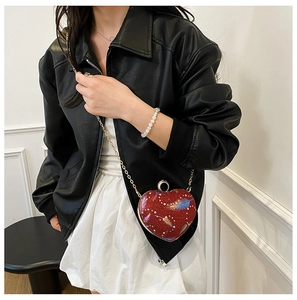 Detail of red heart-shaped sequin handbag with colorful feathers and gold chain
